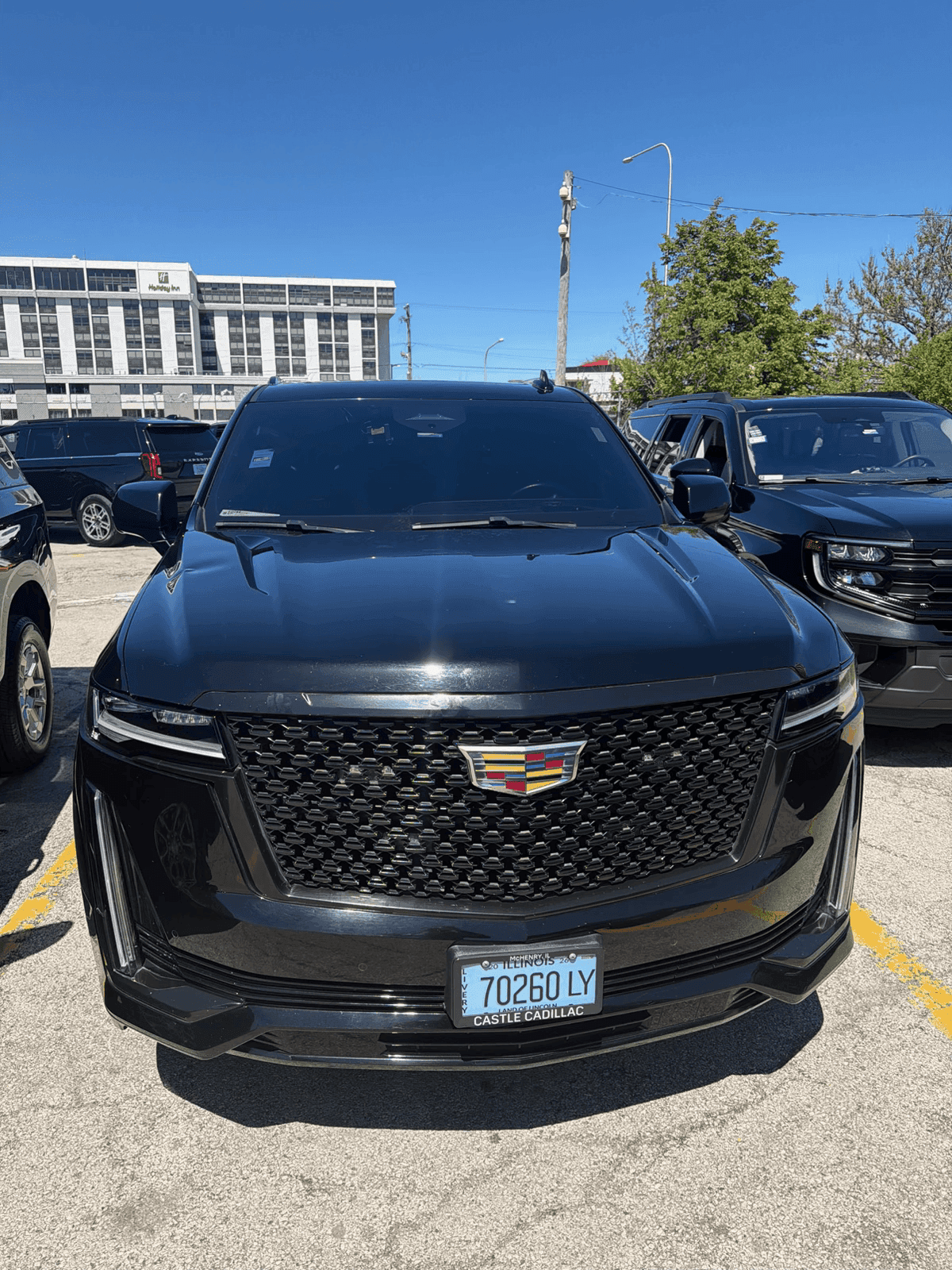 Front view of black Cadillac SUV with a large mesh grille in a sunny lot.