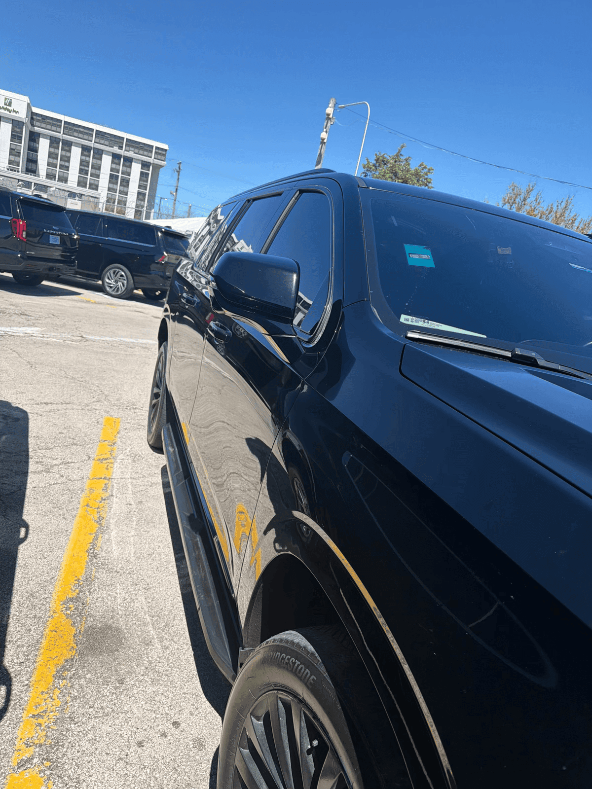 Low-angle side view of a shiny black SUV parked in a sunny outdoor lot.