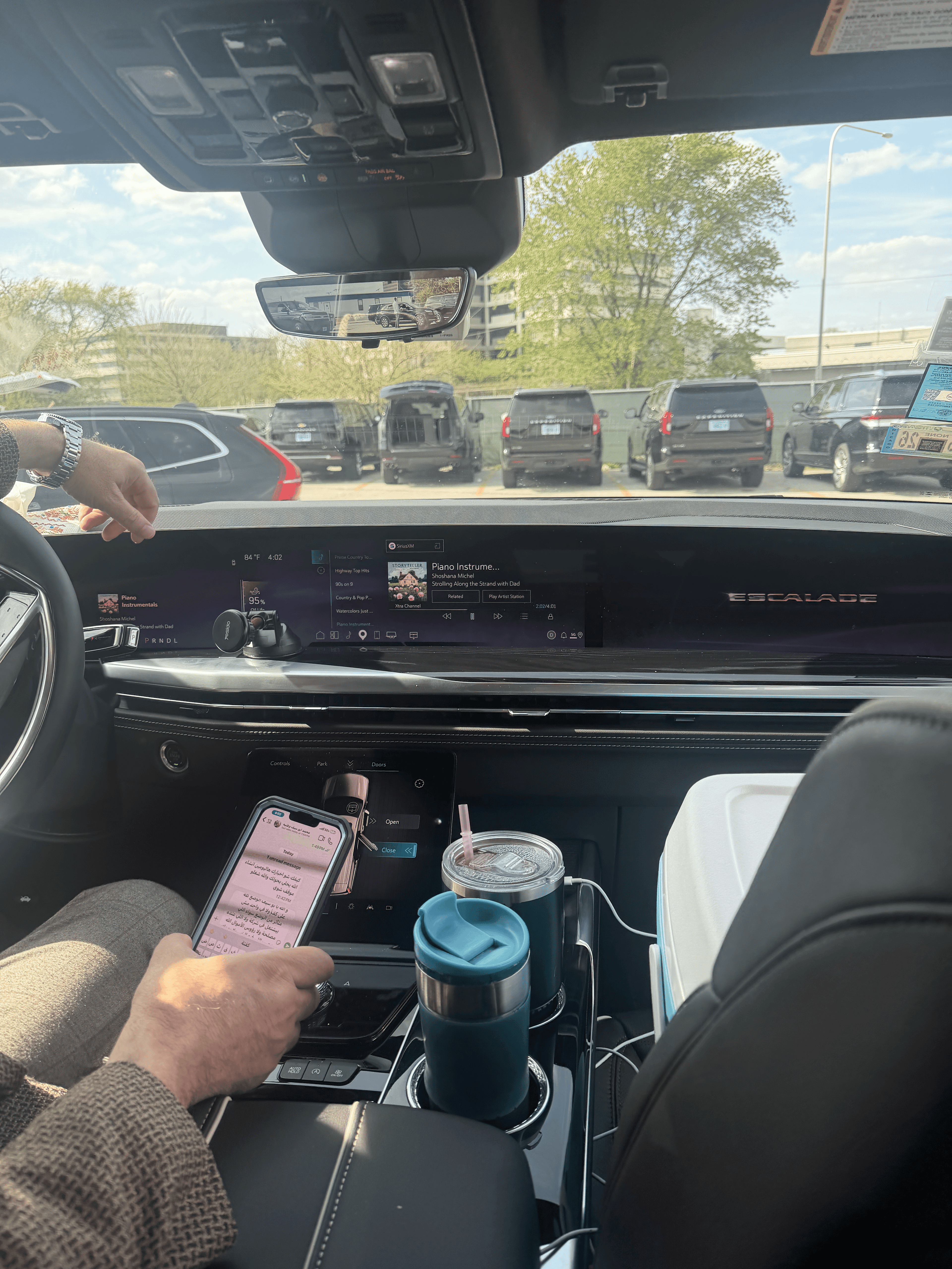 Interior view of a Cadillac Escalade with a digital dashboard, smartphone, and two drink tumblers.
