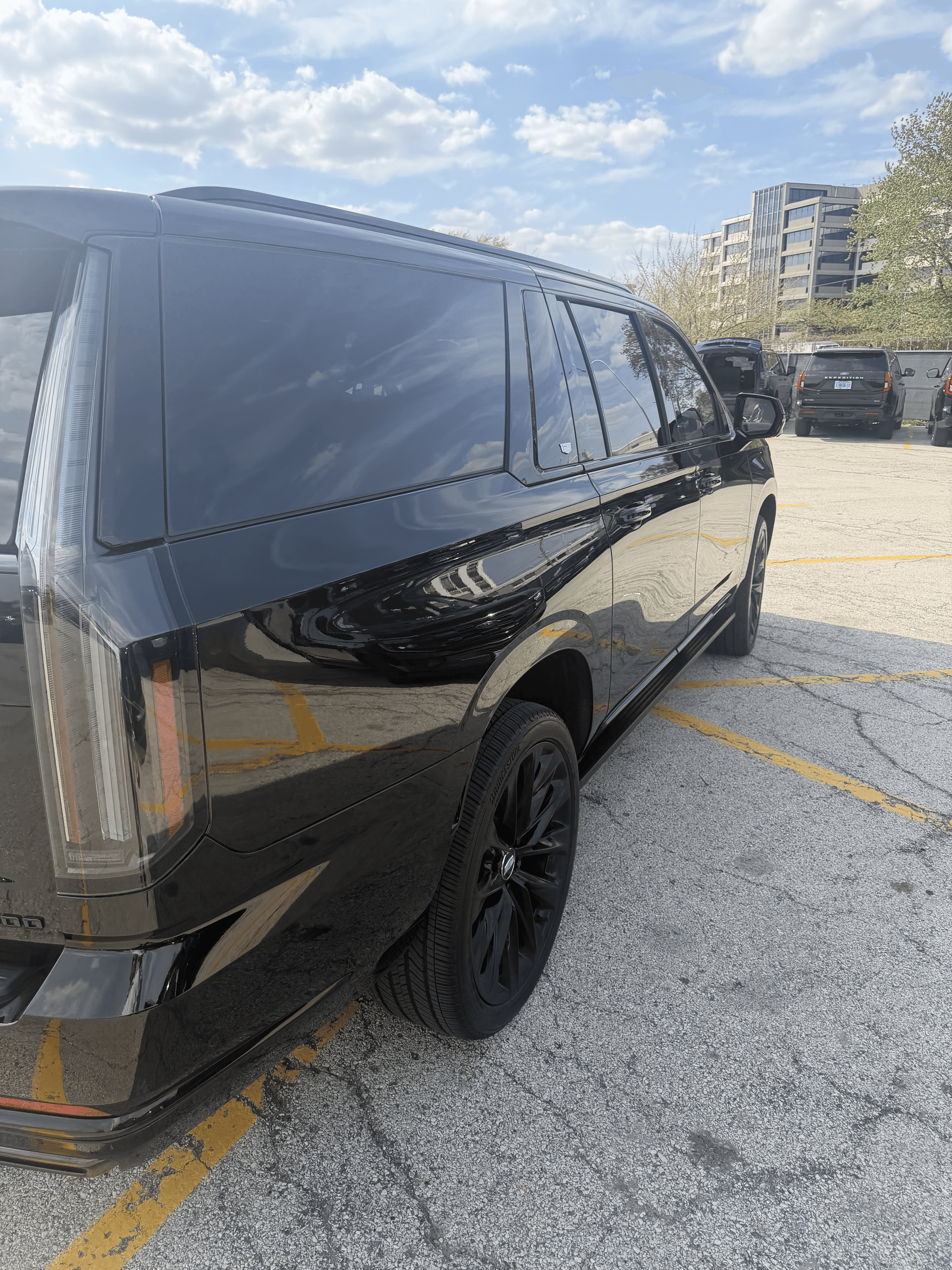 Black Cadillac Escalade with tinted windows and black rims parked in a sunny lot.