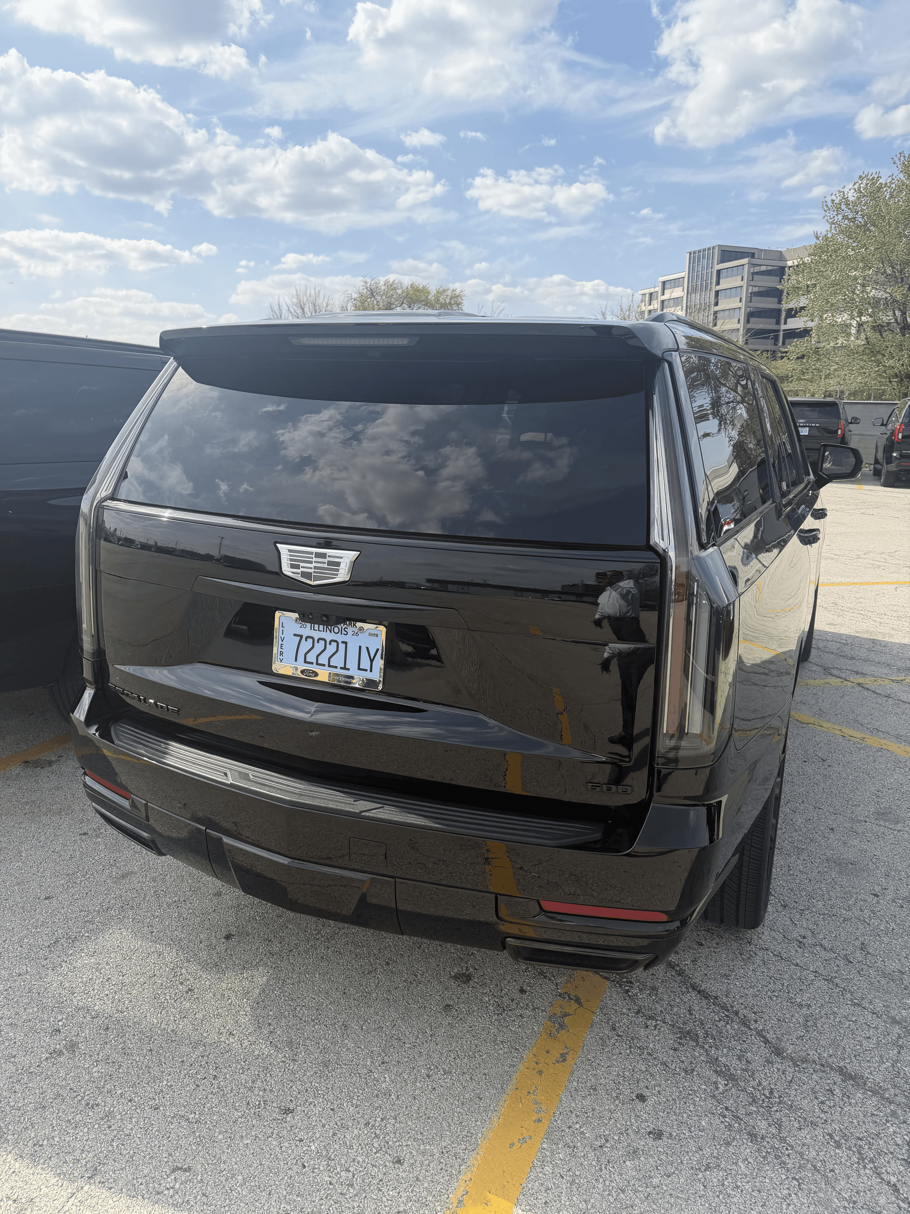Rear view of a black Cadillac Escalade parked in a lot under cloudy skies.