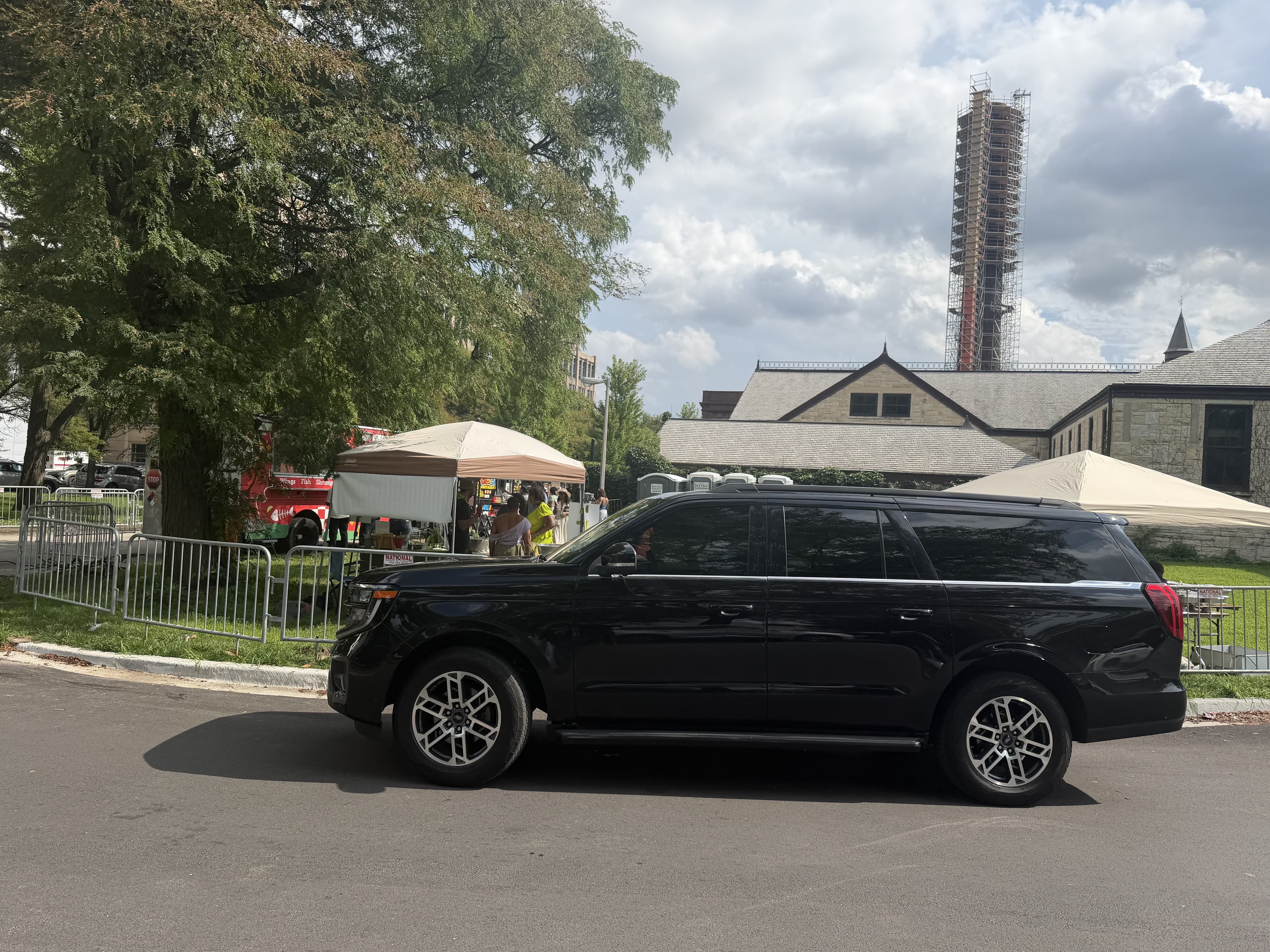 Black SUV parked near outdoor event tents and a tall tower under construction.