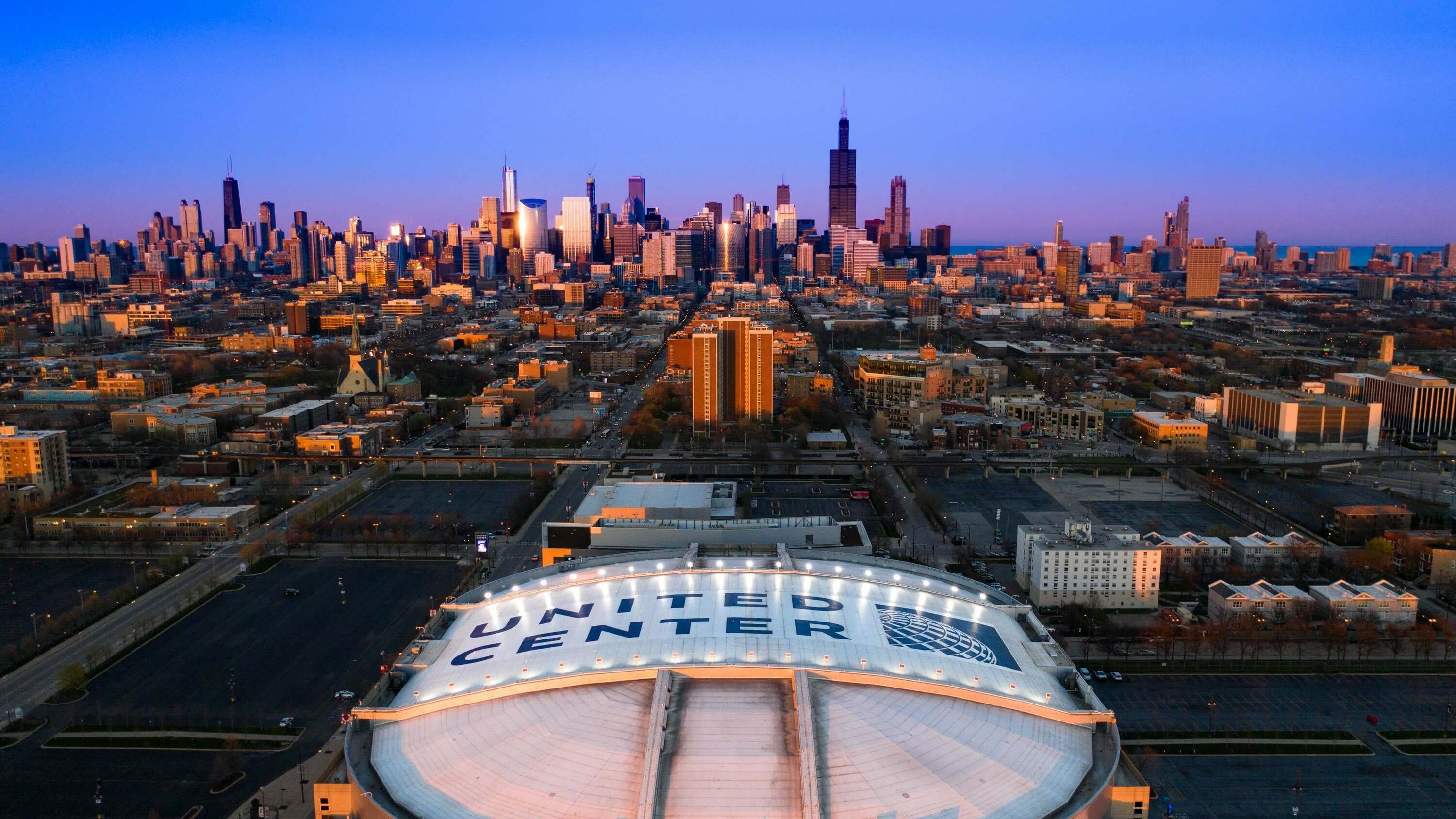 Aerial view of the United Center at sunset with the Chicago skyline in the background.
